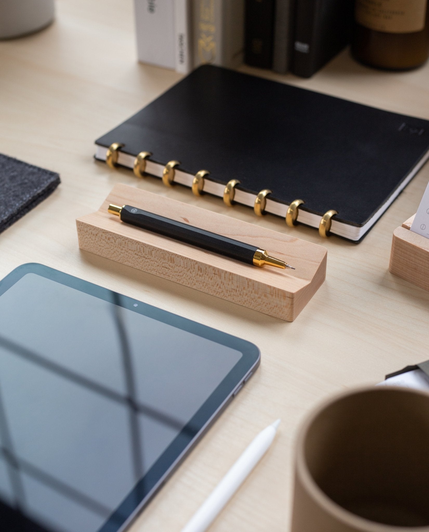 A black and gold pen rests on a Pen Tray (Maple), made in Pennsylvania, next to a black notebook, tablet, white stylus, and brown cup on a tidy desk.