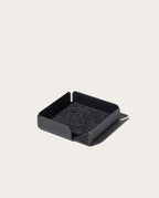 The Gather Note Tray (1x1 - Black) is a sleek black square tray with short sides and a soft, dark felt bottom. Placed against a light background, this elegant Magnetic Desk Organizer helps keep your workspace tidy and clutter-free.