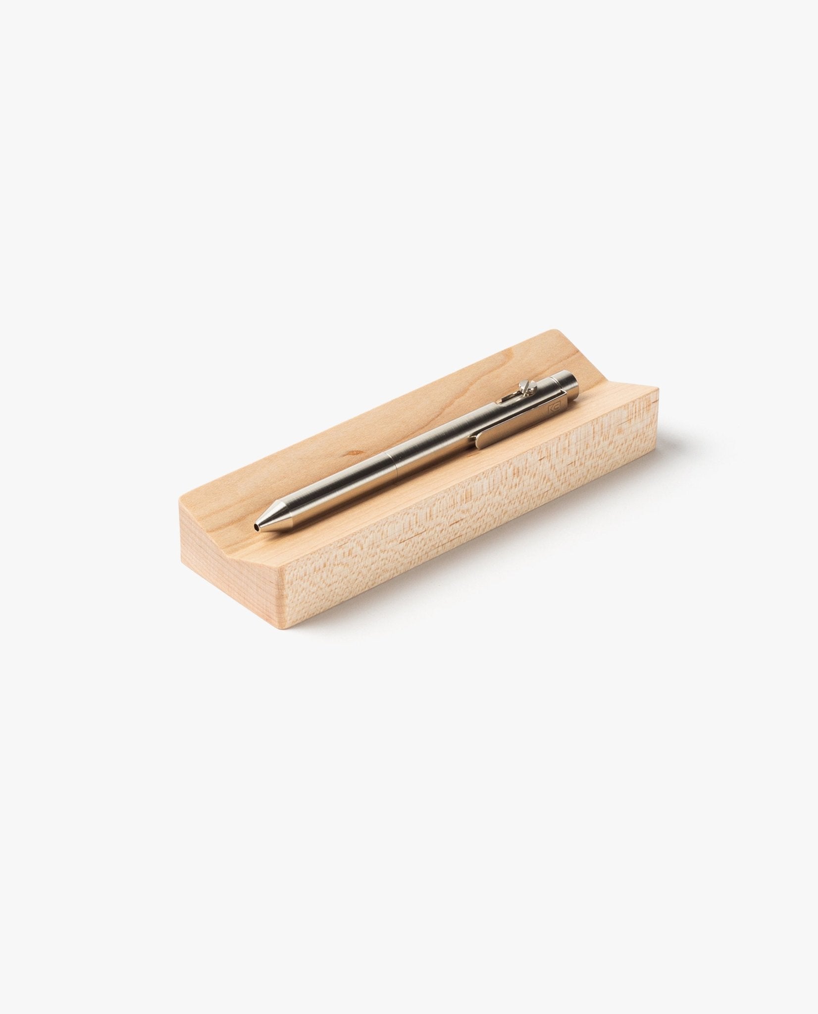 A silver pen rests on the Pen Tray (Maple), a rectangular maple holder with a groove, handcrafted in Pennsylvania, and placed on a white background.