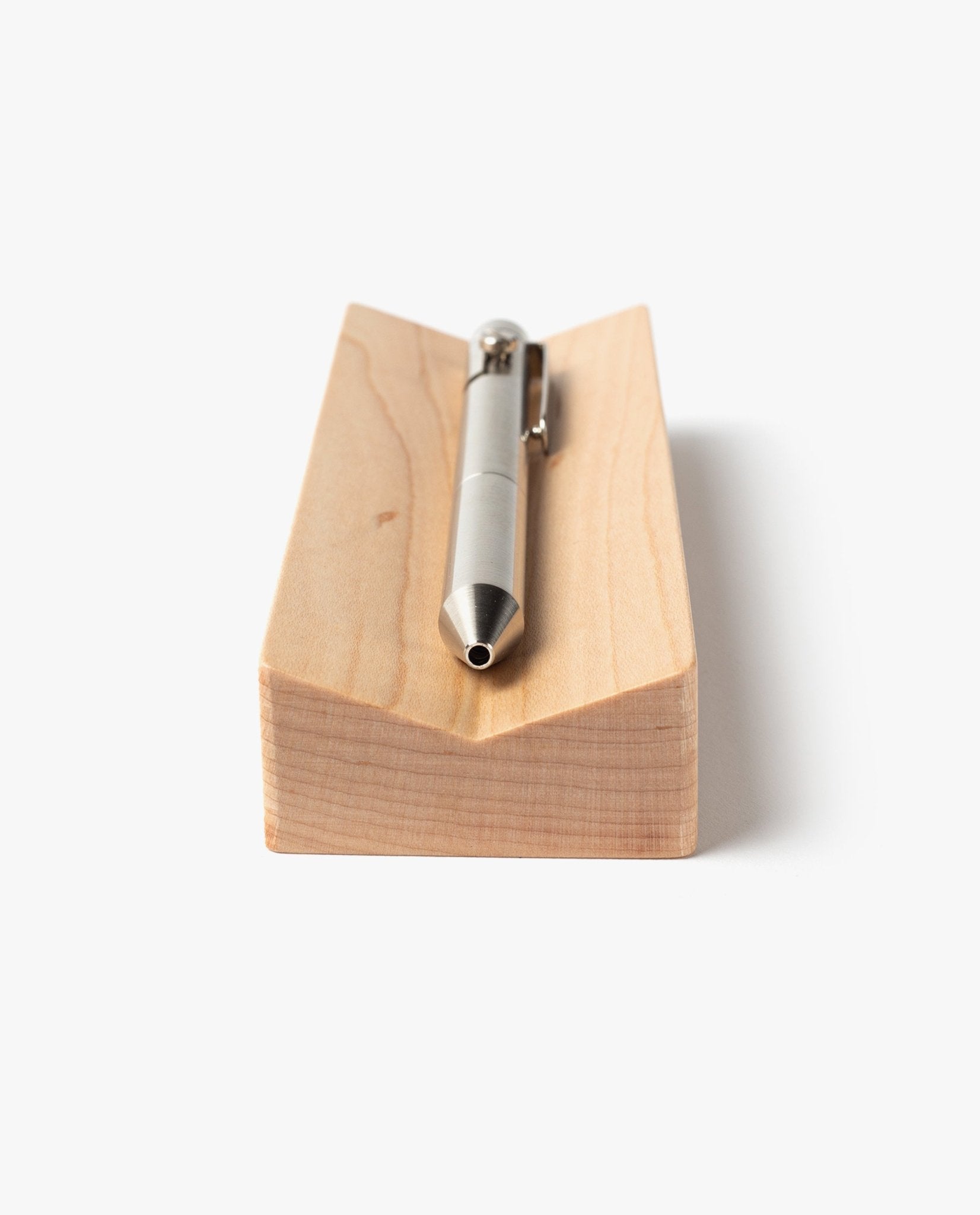 A silver metal pen rests horizontally on the Pen Tray (Maple), a rectangular solid maple block with a groove, shown from the tip-end on a plain white background. This elegant piece is expertly made in Pennsylvania.