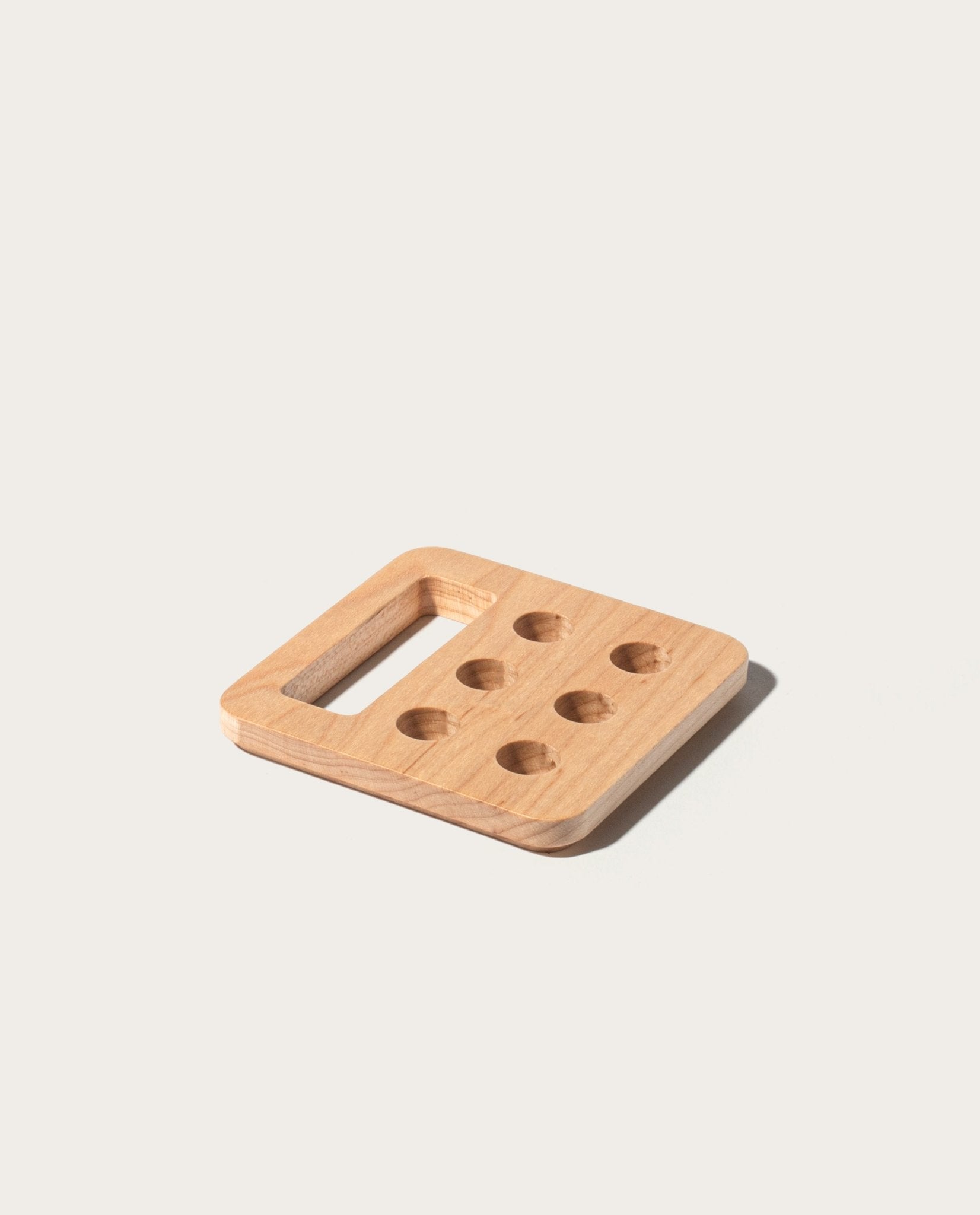 The Gather Pencil Cup Lid (Maple) is a square, solid maple accessory designed with rounded edges, a rectangular cutout on one side, and six circular holes arranged in two rows of three. Made in Pennsylvania, this Warehouse Item is photographed against a plain light background.