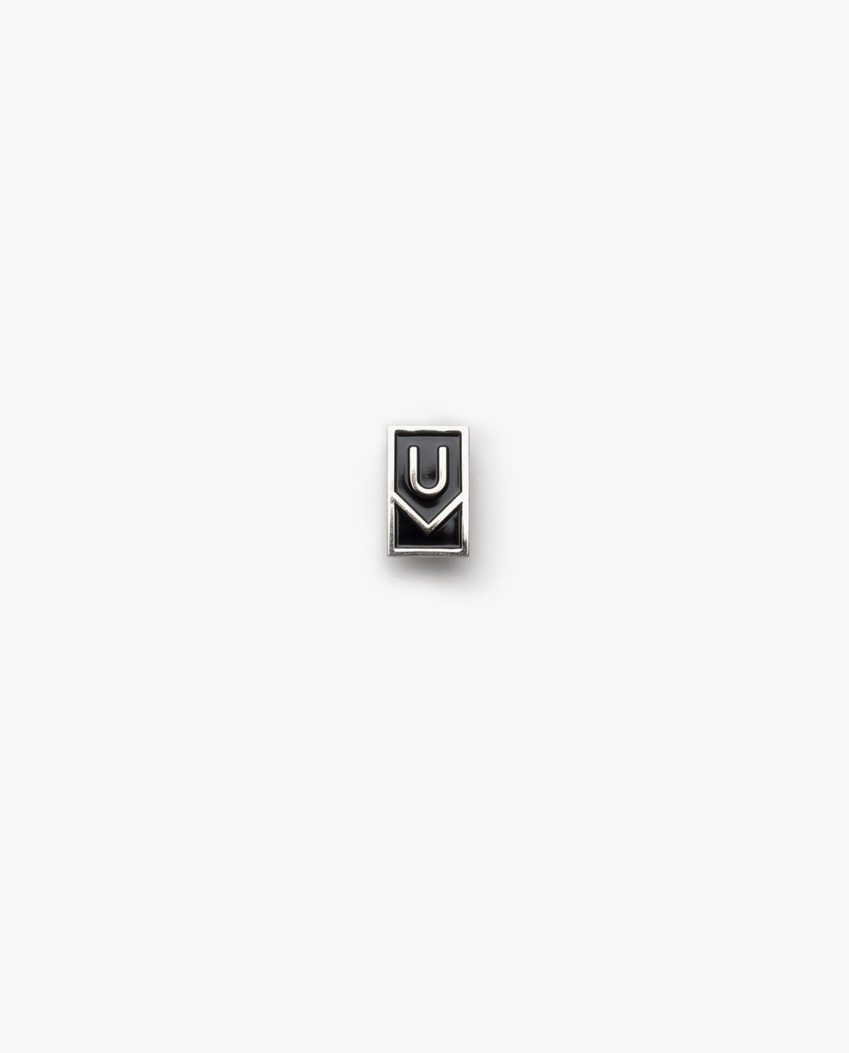 The Ugmonk Enamel Pin is a small, rectangular metallic accessory featuring a minimalist design with geometric U and M shapes on a plain white background.