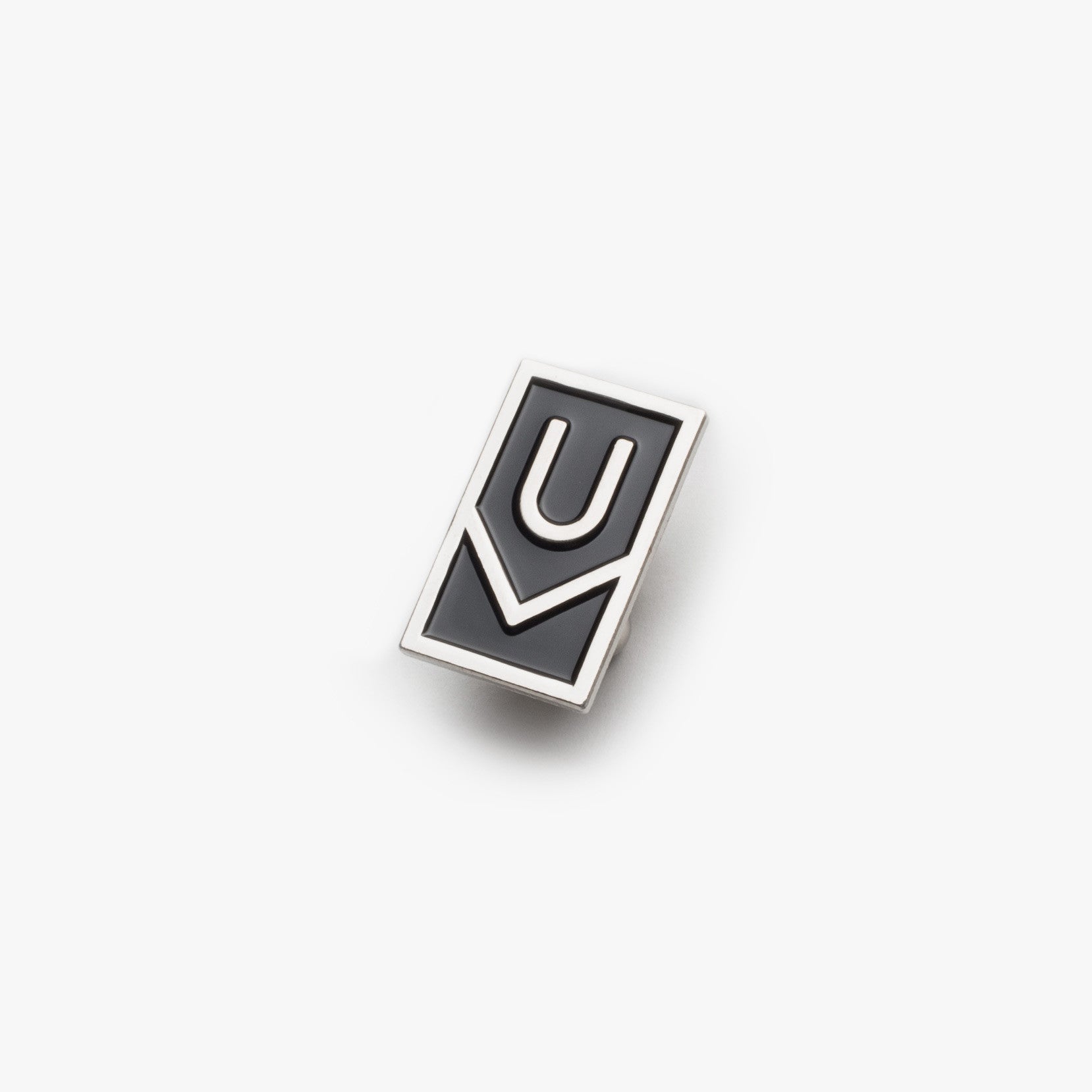 The Ugmonk Enamel Pin features a rectangular black design with a raised silver outline forming a stylized "U" above a check mark, shown against a plain white background.