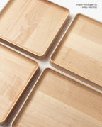 Four medium maple Valet Trays with rounded edges are arranged diagonally on a white surface, displaying unique wood grain patterns. Text in the corner reads, Unique wood grain on every handcrafted Valet Tray (Maple - Medium).