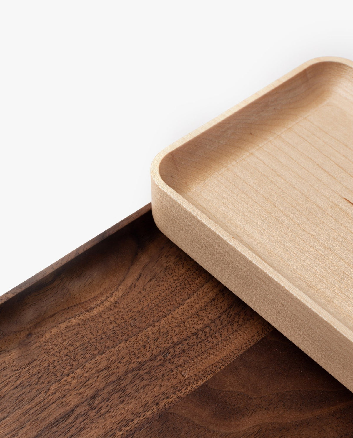 Two rectangular wooden trays overlap on a white background; one handcrafted valet tray (Maple – Small) features light-colored solid maple with rounded corners, while the other tray is darker with visible wood grain.