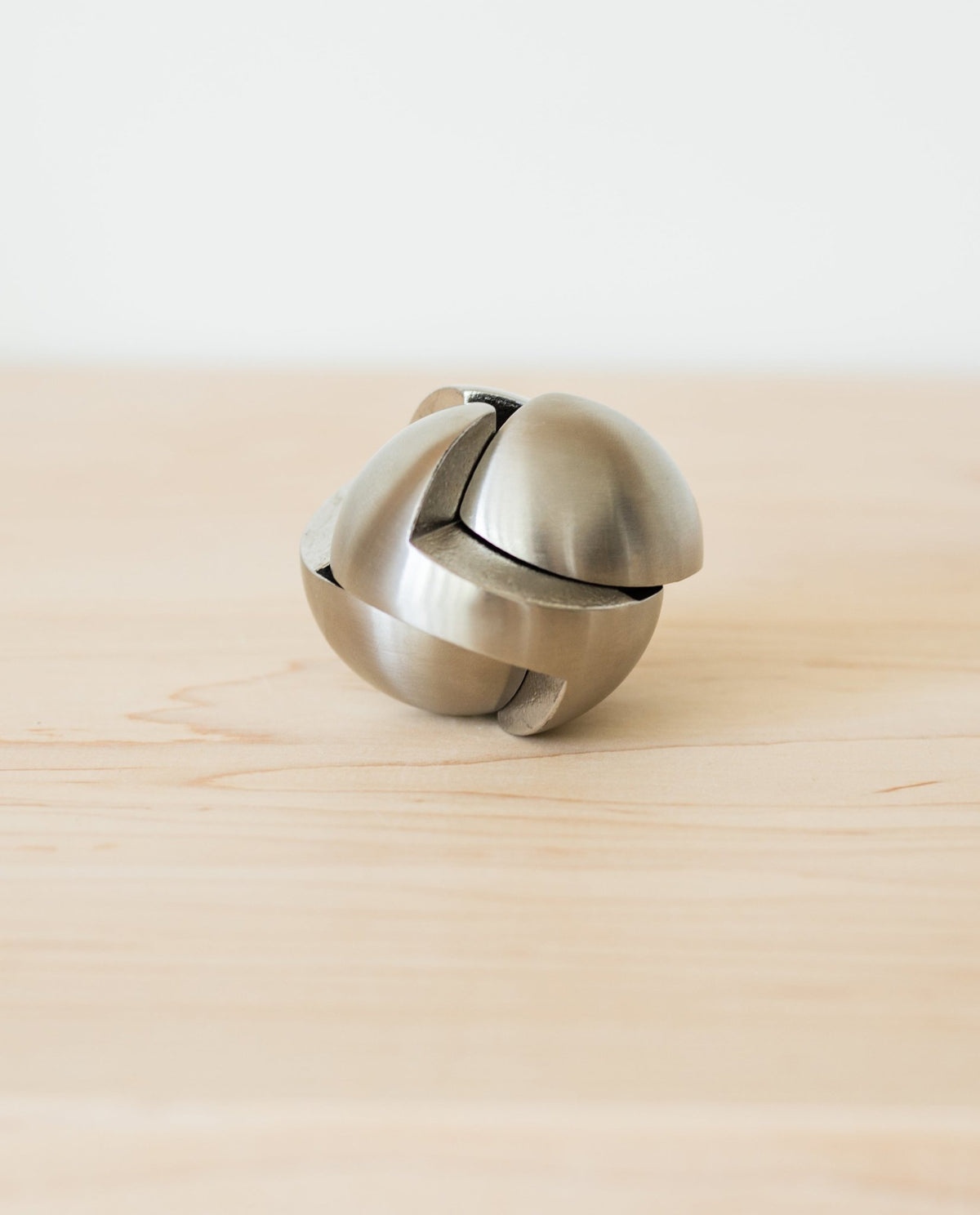 The Craighill Venn Puzzle (Stainless Steel) is displayed assembled on a light wooden surface, its smooth, curved pieces interlocking to form a striking spherical shape reminiscent of this renowned puzzle.