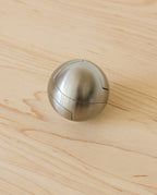 The Craighill Venn Puzzle (Stainless Steel) is a metallic, spherical puzzle with smooth, brushed surfaces and visible interlocking seams, resting on a light wooden surface.